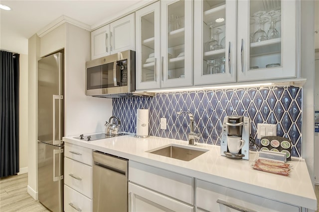 kitchen with white cabinets, appliances with stainless steel finishes, sink, backsplash, and light hardwood / wood-style flooring