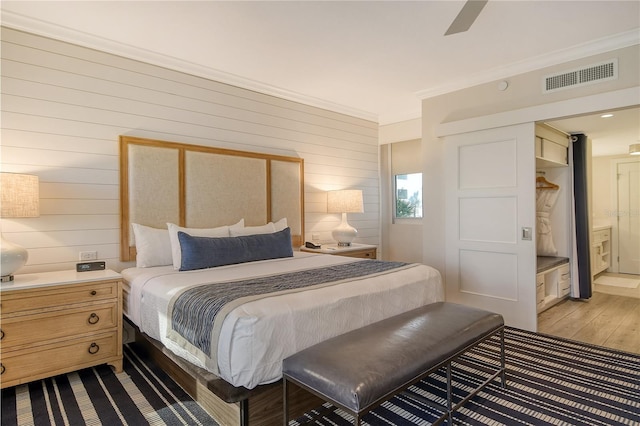 bedroom featuring ceiling fan, ensuite bathroom, crown molding, and wood walls