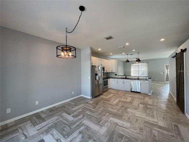 kitchen featuring pendant lighting, light parquet flooring, a barn door, white cabinets, and appliances with stainless steel finishes