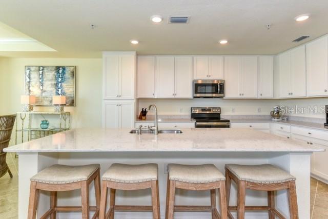 kitchen with sink, stainless steel appliances, a kitchen island with sink, and white cabinetry