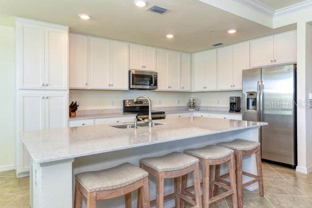 kitchen with stainless steel appliances, an island with sink, light stone countertops, white cabinets, and sink