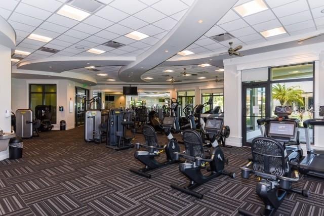 workout area featuring a paneled ceiling, ceiling fan, and dark colored carpet