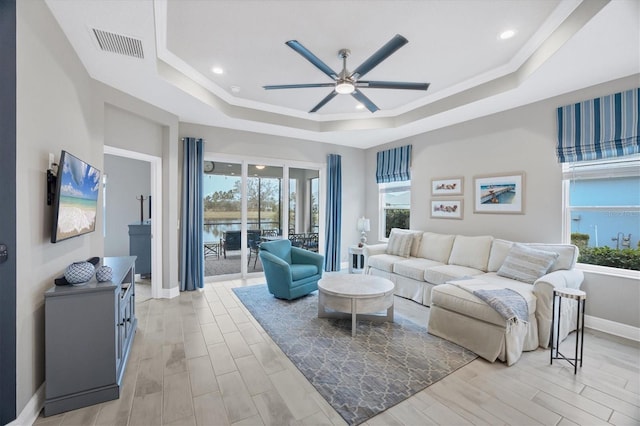 living room featuring a raised ceiling, ceiling fan, and ornamental molding