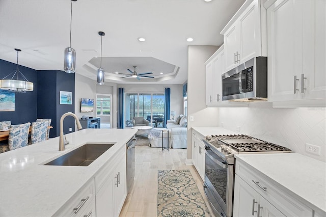 kitchen with hanging light fixtures, a tray ceiling, white cabinets, appliances with stainless steel finishes, and sink