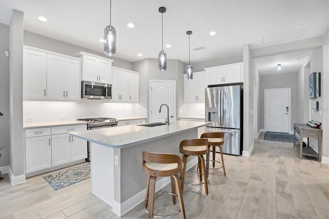 kitchen with decorative light fixtures, stainless steel appliances, a kitchen island with sink, and white cabinets