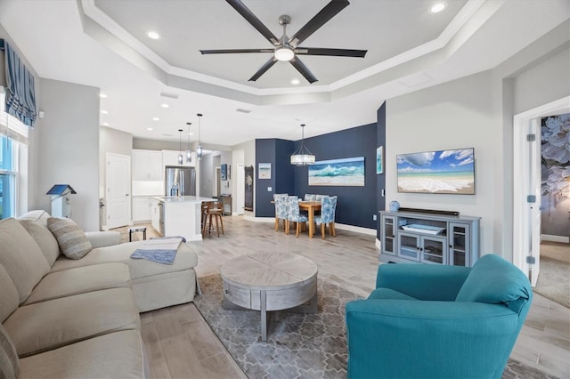 living room with ceiling fan with notable chandelier, a tray ceiling, and crown molding