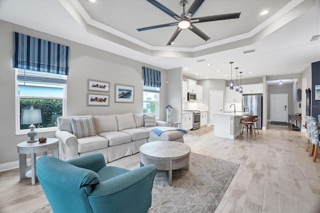 living room featuring ornamental molding, ceiling fan, a tray ceiling, and sink