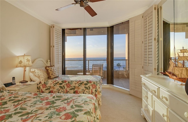 carpeted bedroom featuring access to outside, a water view, ceiling fan, expansive windows, and crown molding