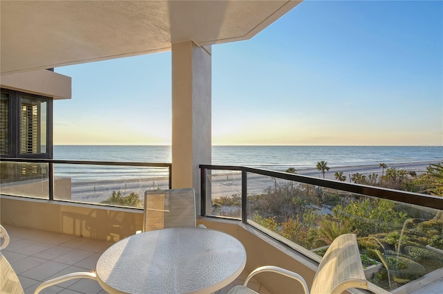 balcony at dusk featuring a beach view and a water view