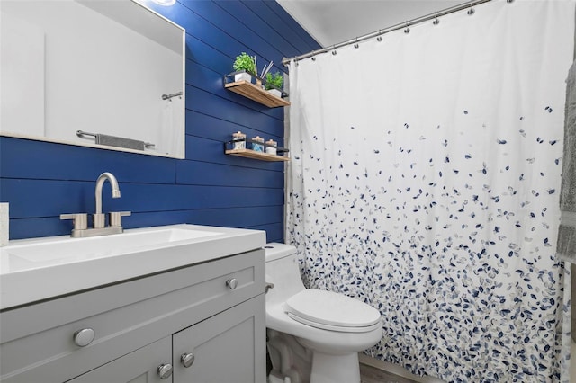 bathroom featuring wooden walls, vanity, and toilet