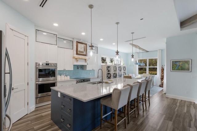 kitchen featuring sink, stainless steel appliances, white cabinets, decorative light fixtures, and a center island with sink