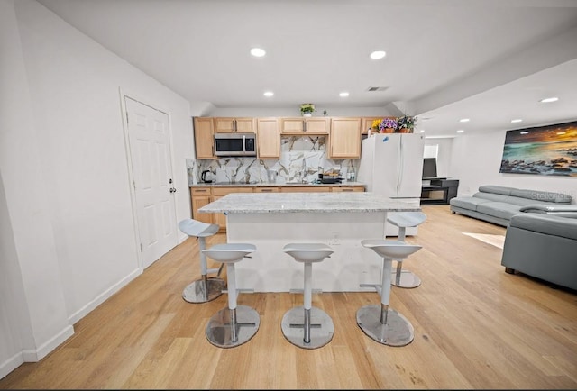 kitchen with a kitchen breakfast bar, light brown cabinetry, backsplash, a center island, and white fridge
