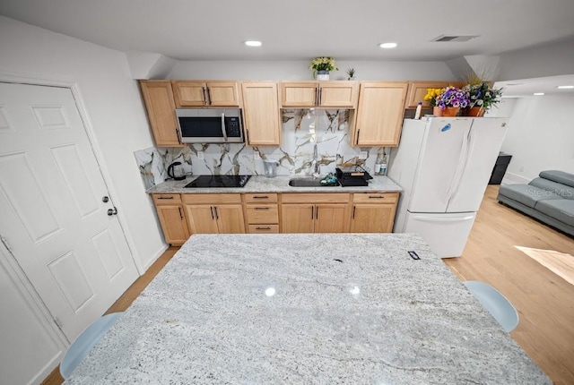 kitchen with light brown cabinets, light stone counters, black electric cooktop, decorative backsplash, and white fridge