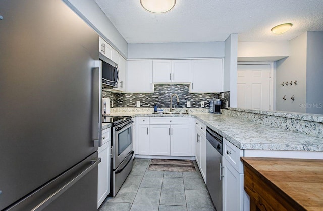 kitchen featuring a textured ceiling, light tile patterned floors, white cabinets, appliances with stainless steel finishes, and sink