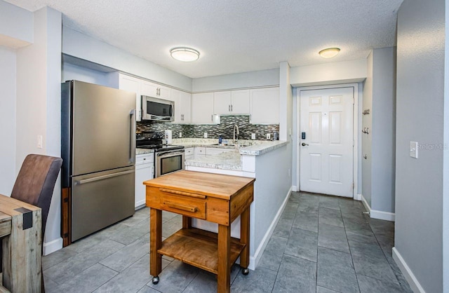 kitchen featuring a textured ceiling, decorative backsplash, white cabinetry, appliances with stainless steel finishes, and sink