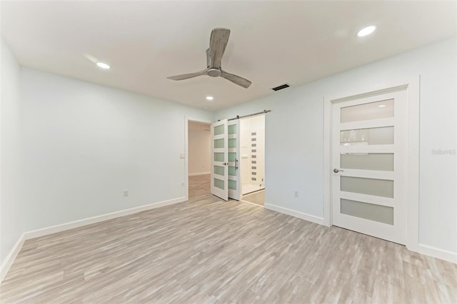 spare room with ceiling fan, a barn door, and light hardwood / wood-style flooring