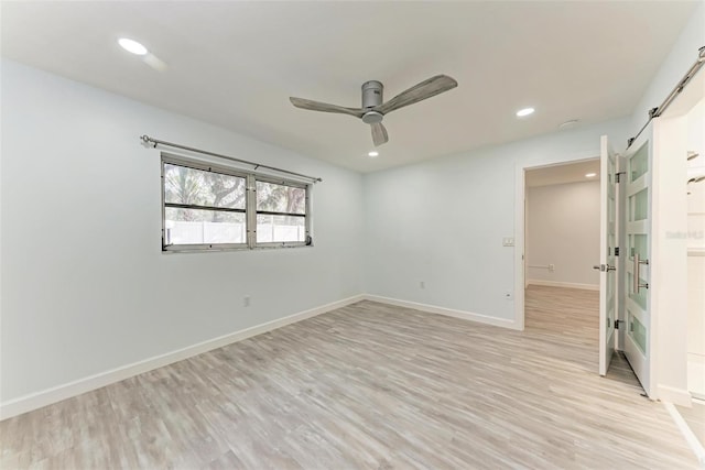 unfurnished room featuring ceiling fan, light wood-type flooring, and a barn door