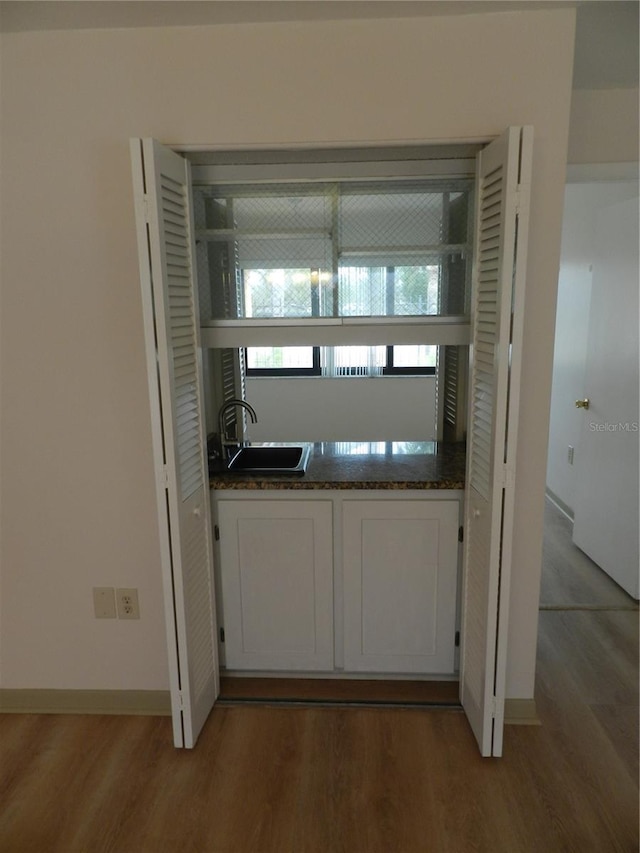 kitchen with light wood finished floors, baseboards, white cabinetry, and a sink