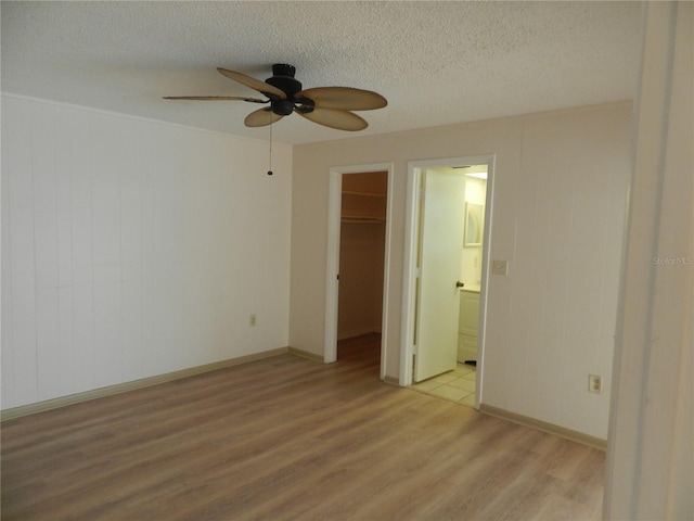 unfurnished bedroom with a textured ceiling, light wood-style flooring, a closet, a walk in closet, and ensuite bath