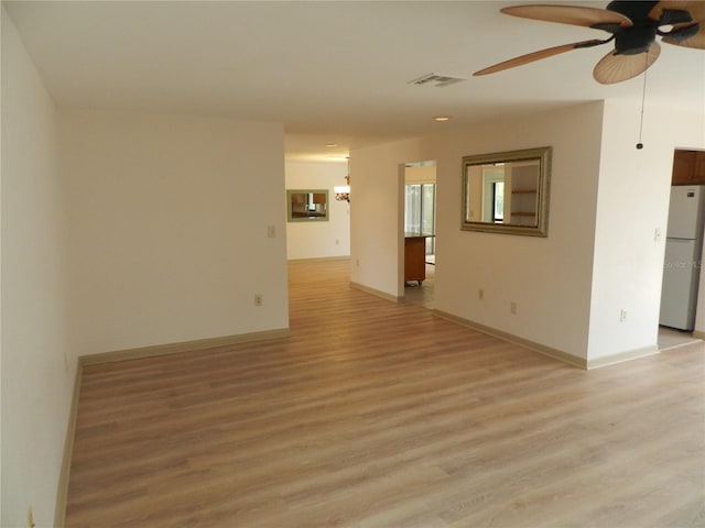 empty room featuring ceiling fan, light wood finished floors, visible vents, and baseboards