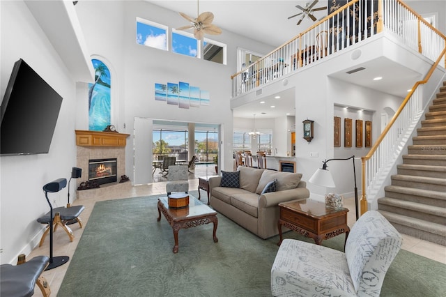 tiled living room with ceiling fan, a towering ceiling, and a tile fireplace