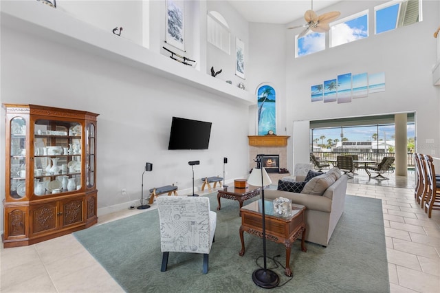 living room featuring ceiling fan, light tile patterned floors, a towering ceiling, and a fireplace