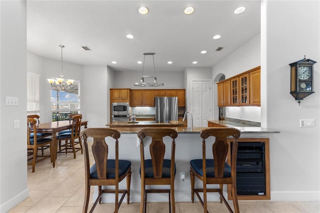 kitchen featuring pendant lighting, appliances with stainless steel finishes, dark stone countertops, an inviting chandelier, and kitchen peninsula