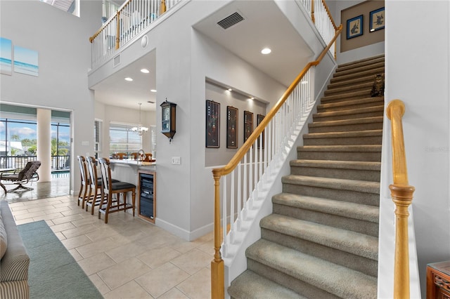 stairs featuring an inviting chandelier, tile patterned floors, a towering ceiling, and beverage cooler