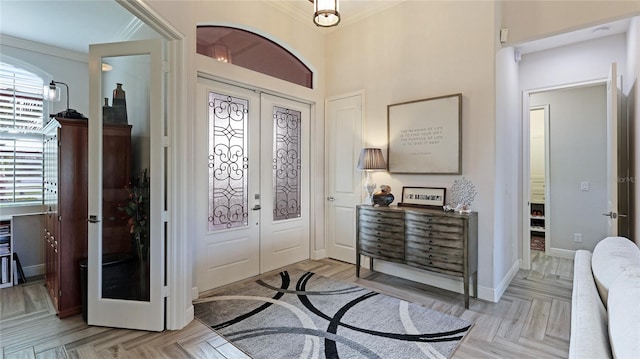 entryway with french doors, crown molding, and light parquet floors