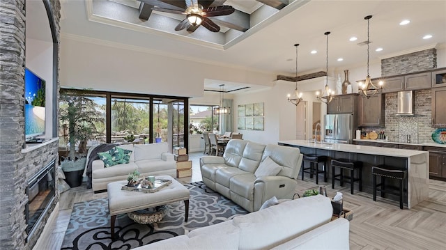 living room with a high ceiling, light parquet flooring, crown molding, ceiling fan, and a stone fireplace