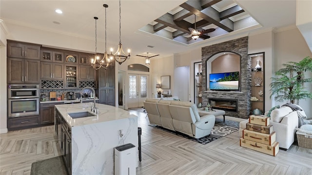 kitchen featuring coffered ceiling, an island with sink, light stone countertops, light parquet floors, and sink