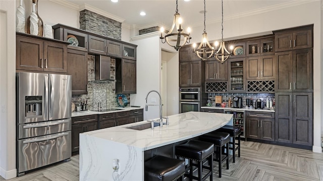 kitchen featuring sink, backsplash, light stone countertops, a kitchen island with sink, and appliances with stainless steel finishes