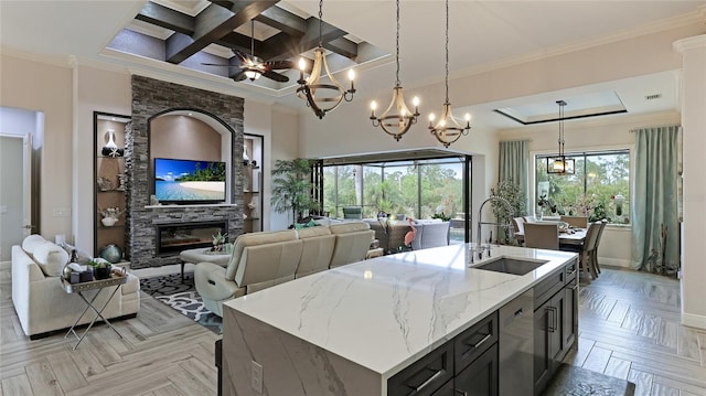 kitchen with coffered ceiling, light parquet flooring, an island with sink, light stone countertops, and sink