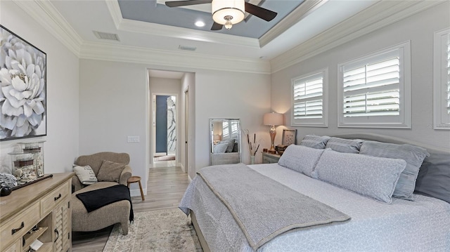 bedroom with ornamental molding, ceiling fan, a tray ceiling, and light hardwood / wood-style floors