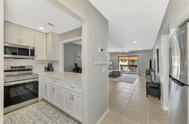 kitchen with white cabinets, stainless steel appliances, backsplash, ceiling fan, and light tile patterned floors