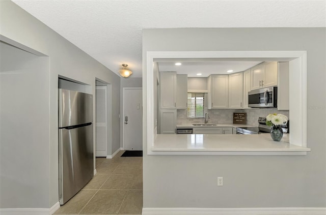 kitchen featuring a textured ceiling, appliances with stainless steel finishes, white cabinetry, backsplash, and light tile patterned floors