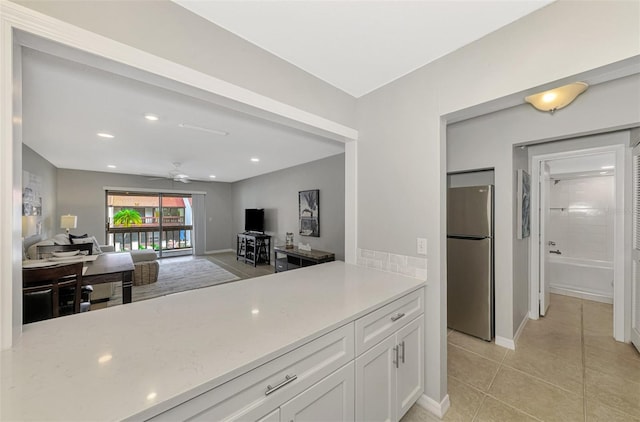 kitchen with ceiling fan, stainless steel refrigerator, light tile patterned flooring, light stone countertops, and white cabinets