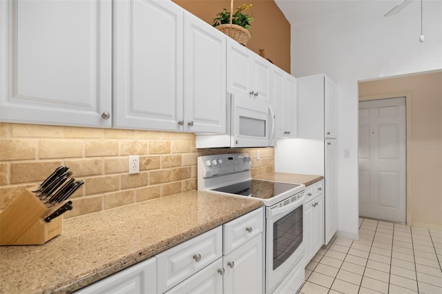 kitchen with decorative backsplash, light tile patterned flooring, white appliances, white cabinets, and light stone counters