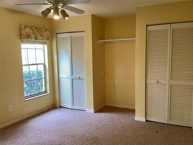 unfurnished bedroom with a textured ceiling, two closets, ceiling fan, and carpet