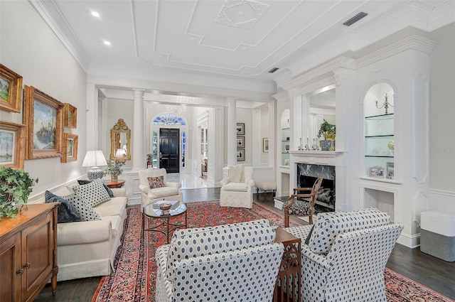 living room featuring wood finished floors, visible vents, decorative columns, a fireplace, and crown molding