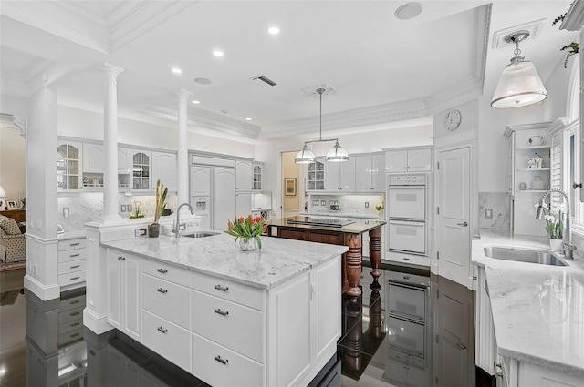 kitchen featuring a sink, decorative columns, and a large island with sink