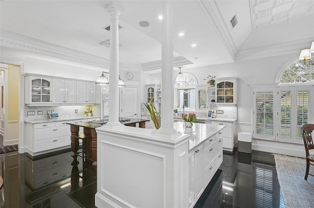 kitchen featuring white cabinetry, glass insert cabinets, ornate columns, and ornamental molding