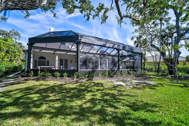 rear view of property with glass enclosure, a chimney, a yard, and a ceiling fan