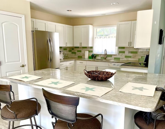 kitchen featuring a kitchen breakfast bar, white cabinetry, sink, and stainless steel refrigerator