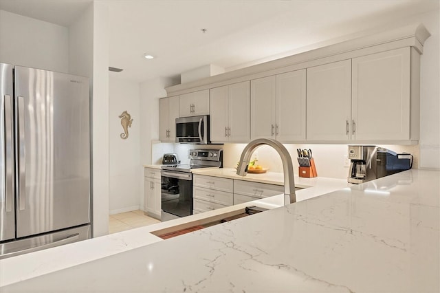 kitchen with stainless steel appliances, white cabinetry, and light stone countertops