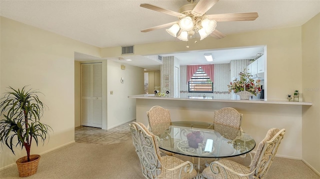 dining space featuring ceiling fan, light colored carpet, and a textured ceiling