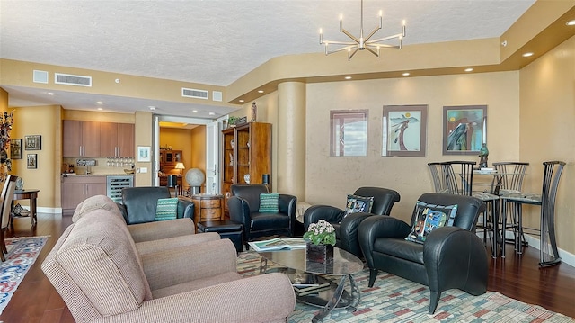 living room with wine cooler, a notable chandelier, dark wood-type flooring, a textured ceiling, and decorative columns