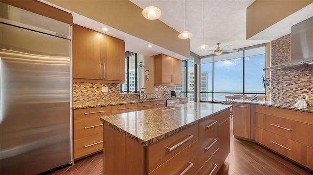 kitchen featuring stainless steel appliances, pendant lighting, a kitchen island, decorative backsplash, and wall chimney range hood