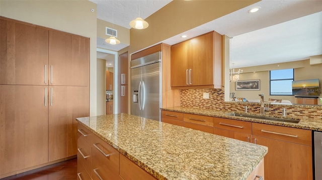 kitchen with light stone countertops, stainless steel built in fridge, pendant lighting, sink, and backsplash