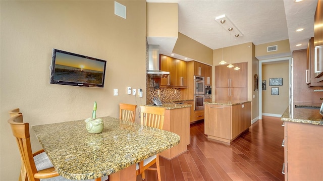 kitchen featuring a center island, wall chimney exhaust hood, tasteful backsplash, stainless steel double oven, and a breakfast bar